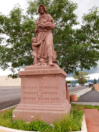 A snapshot of a statue of a woman holding a baby with a young child clinging to her skirts.