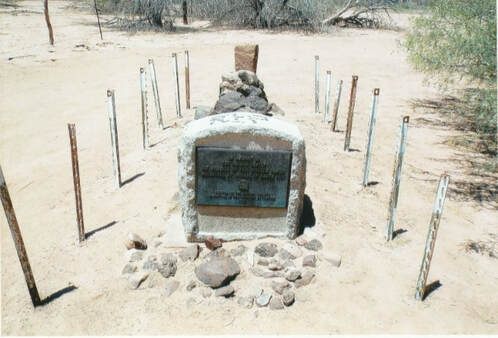 A snapshot of the same marker showing it situated in what may be a burial site in a desert scene.