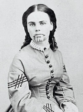 A studio photographic portrait identified as Olive Oatman, a young woman wearing a mid-nineteenth century dress. She has vertical lines tattooed on her chin.