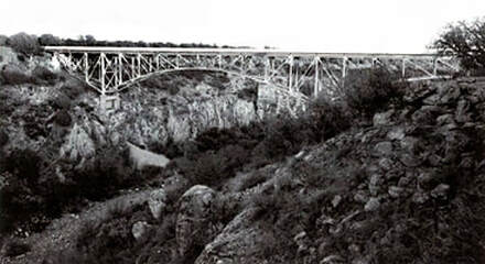 A vintage snapshot of a rocky canyon with a steel bridge.