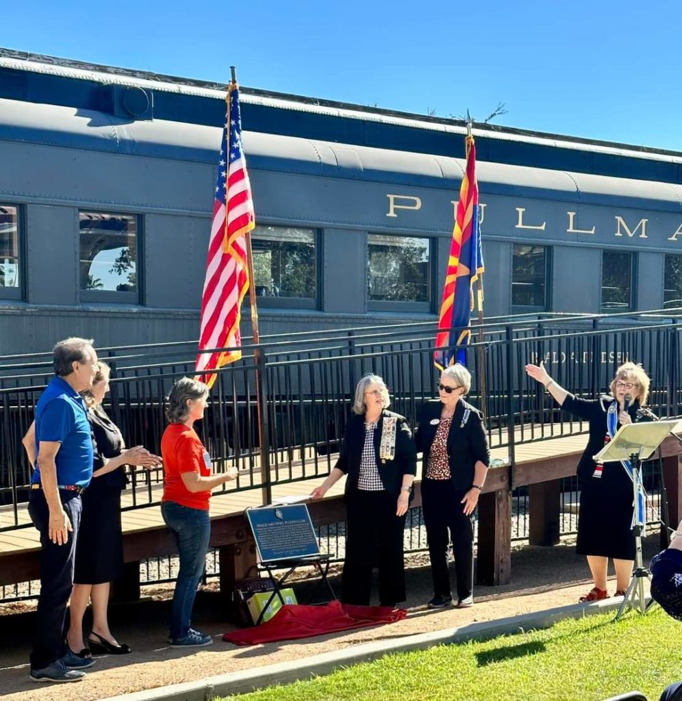 A snapshot of six people standing in front of the Pullman Car. The plaque is displayed on a chair.