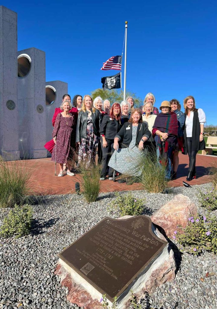 A snapshot of the marker in the foreground and about fifteen adults gathered in the mid-ground. Three of the pillars are visible in the background.