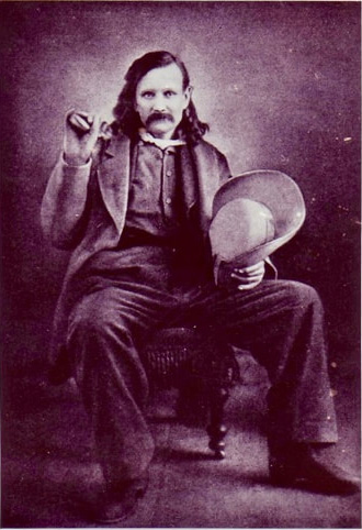 A studio photographic portrait of John “Jack” Swilling, seated, holding a pistol and hat.