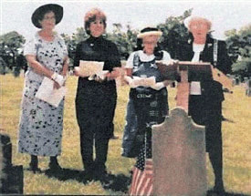 A snapshot of four people standing in front of an upright gravestone.